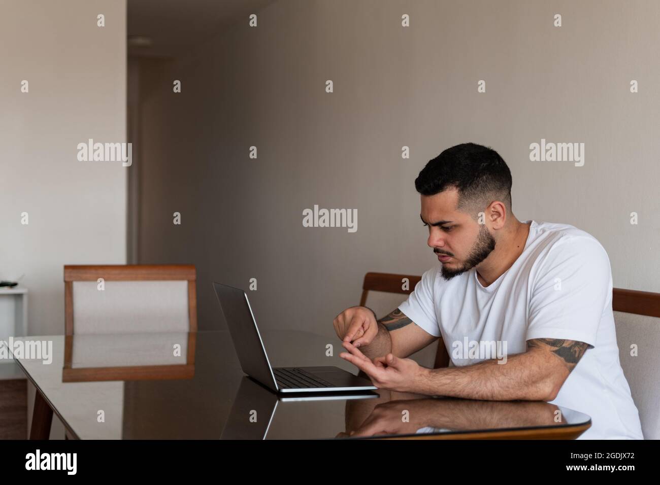 Jeune Latino homme avec des tatouages comptant sur ses doigts devant un ordinateur portable avec un visage sérieux Banque D'Images