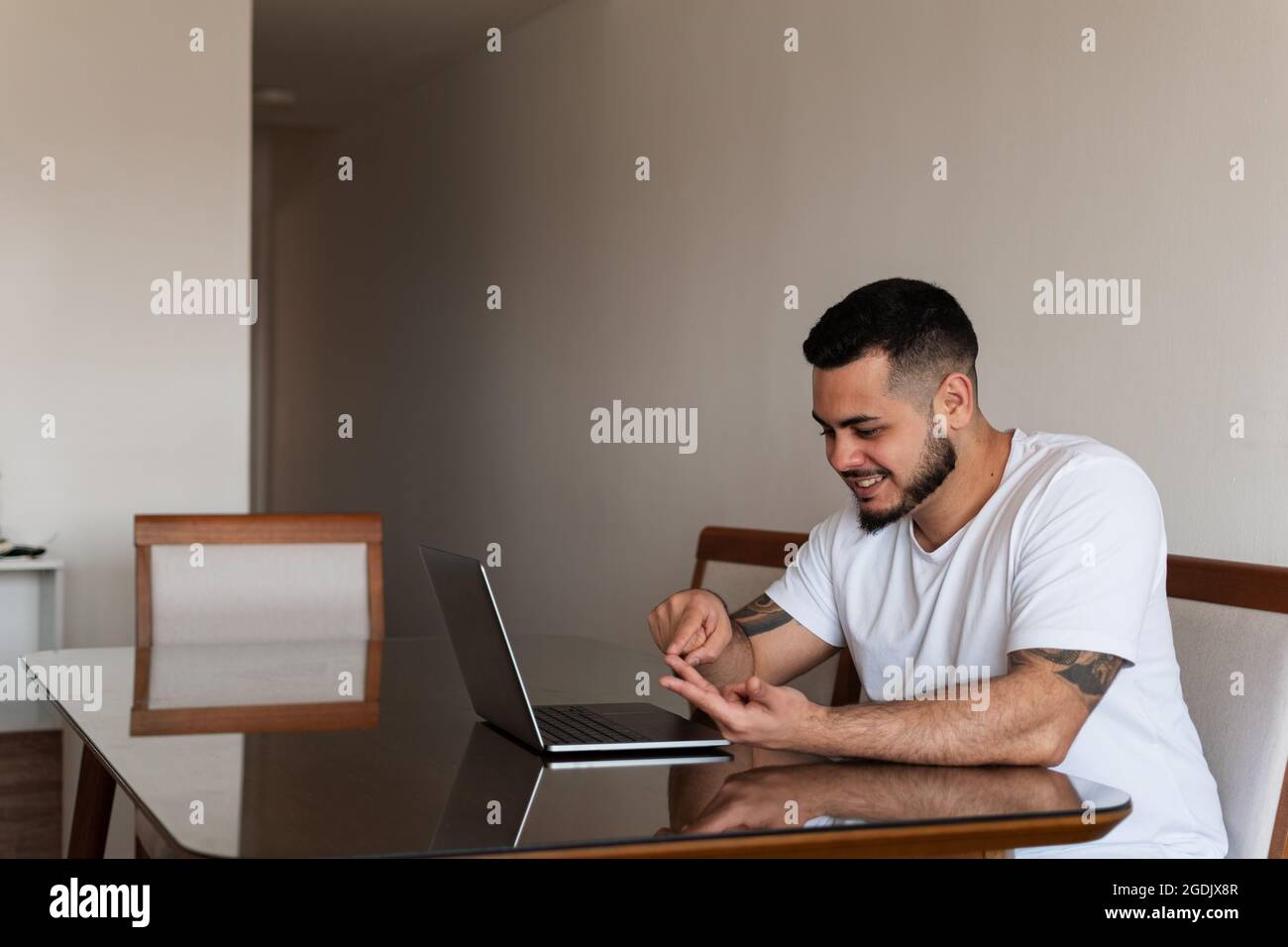 Jeune latin mec avec tatouages souriant et comptant sur ses doigts devant l'ordinateur portable Banque D'Images
