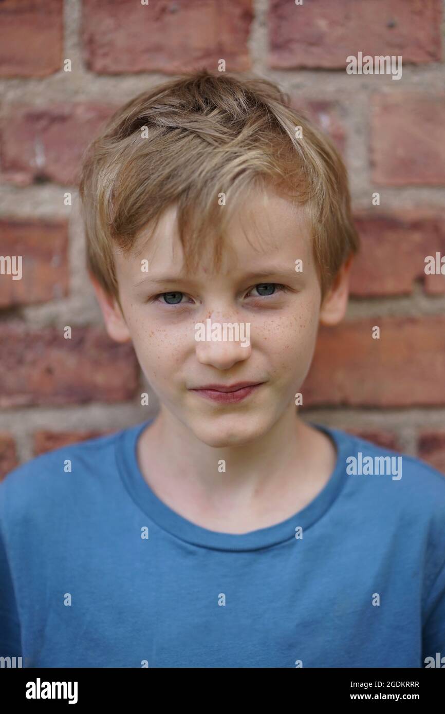 Portrait d'un beau garçon blond de 11 ans avec un t-shirt bleu contre un mur de briques Banque D'Images