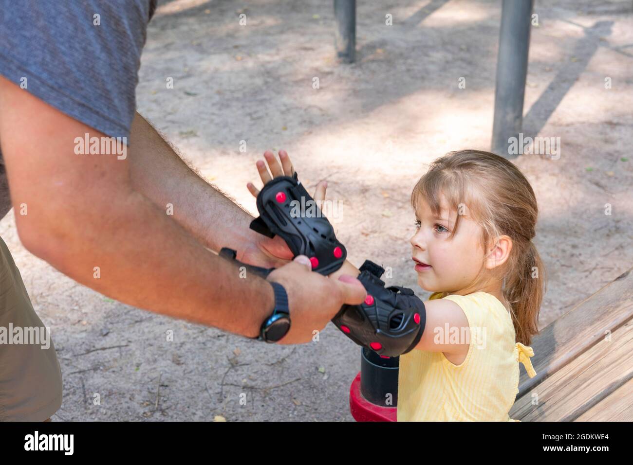 papa met des protège-coudes pour petite fille pour le patinage à roulettes ou le skateboard. Enfant dans des vêtements de sport de protection Banque D'Images