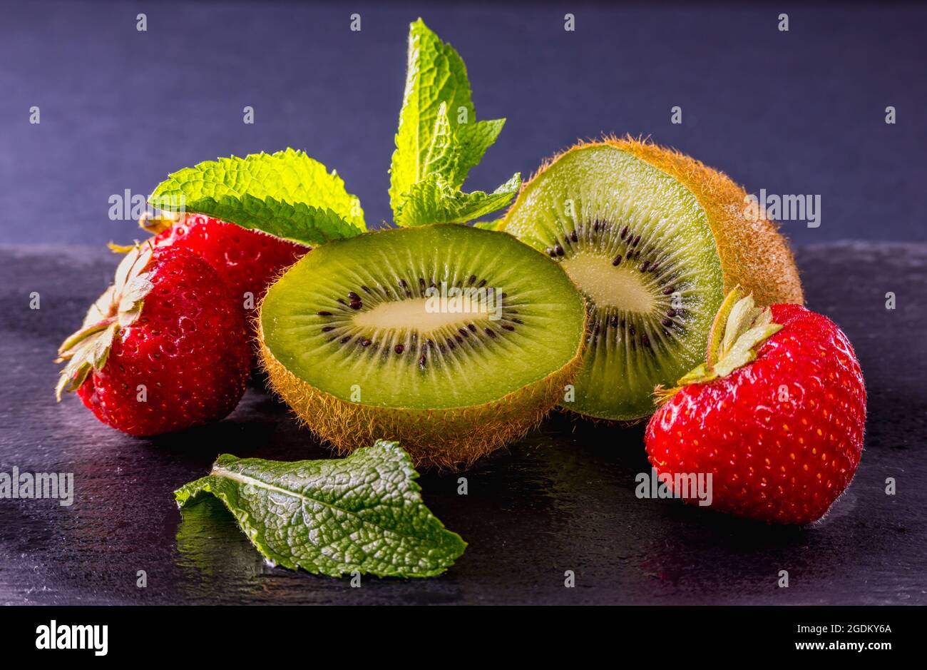 Une photo encore vivant de fruits frais mûrs décorés de feuilles de menthe sur fond sombre et de réflexions sur une table humide. Produits naturels, récolte. Banque D'Images