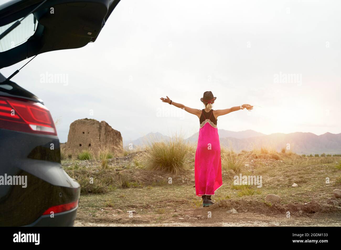 vue arrière jeune femme asiatique voyageur de voiture en robe rouge appréciant la lumière du soleil du matin sur la route Banque D'Images