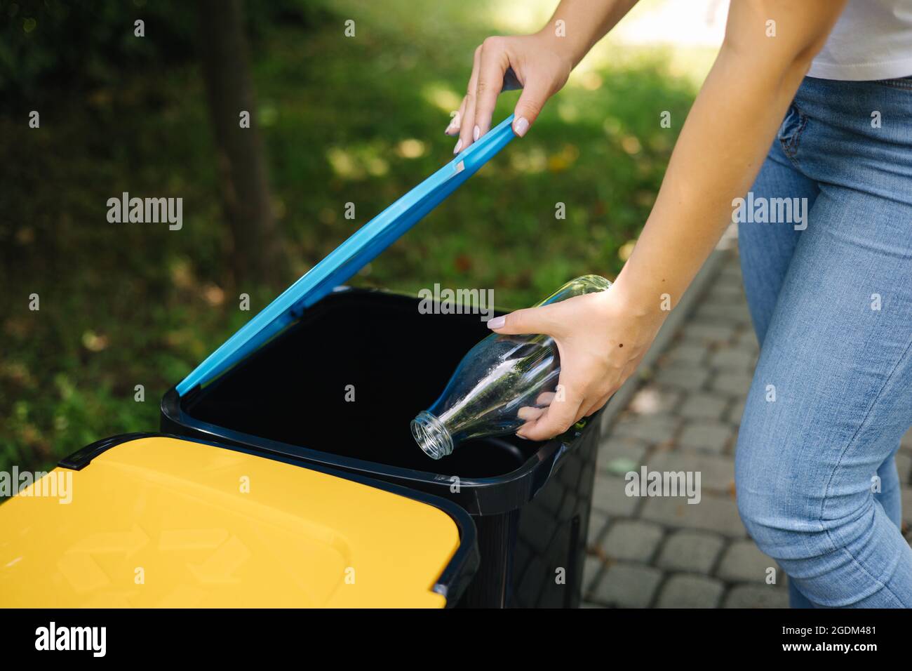 Gros plan portrait femme main throwig bouteille de verre vide dans le bac de recyclage. Différentes couleurs de bacs en plastique dans le parc Banque D'Images