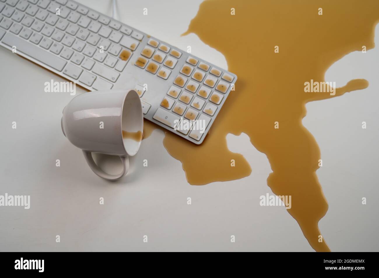 Tasse de café noir renversée sur le clavier de l'ordinateur sur la table blanche. Banque D'Images Tasse de café noir renversée sur le clavier de l'ordinateur sur la table blanche. Banque D'Images
