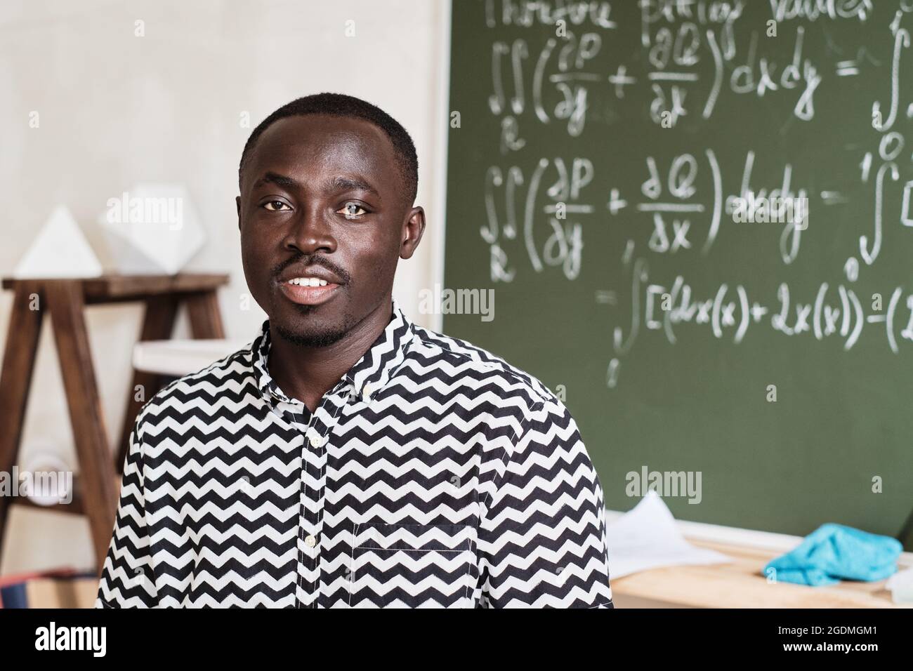 Portrait d'un jeune enseignant africain souriant à la caméra tout en étant  debout dans la salle de classe Photo Stock - Alamy