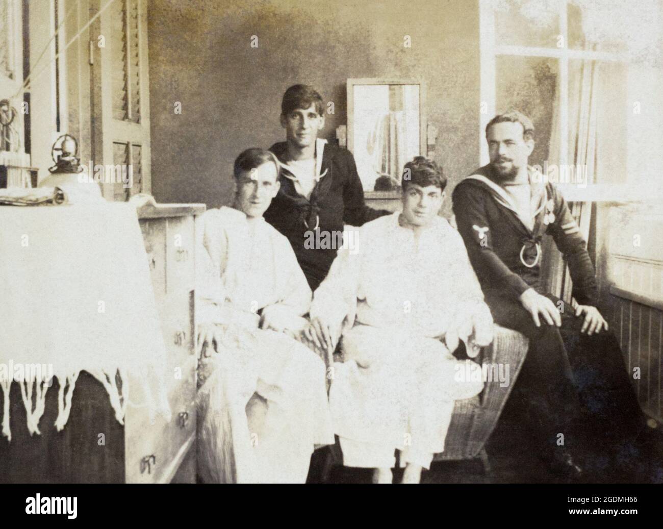 Deux salileurs de la Marine royale britannique rendant visite à deux patients de l'hôpital assis sur un canapé par une fenêtre ouverte. Le marin de droite a insgina d'un Stoker, avec deux longues bandes de service/bonne conduite, et deux médailles. c. Première Guerre mondiale. Banque D'Images