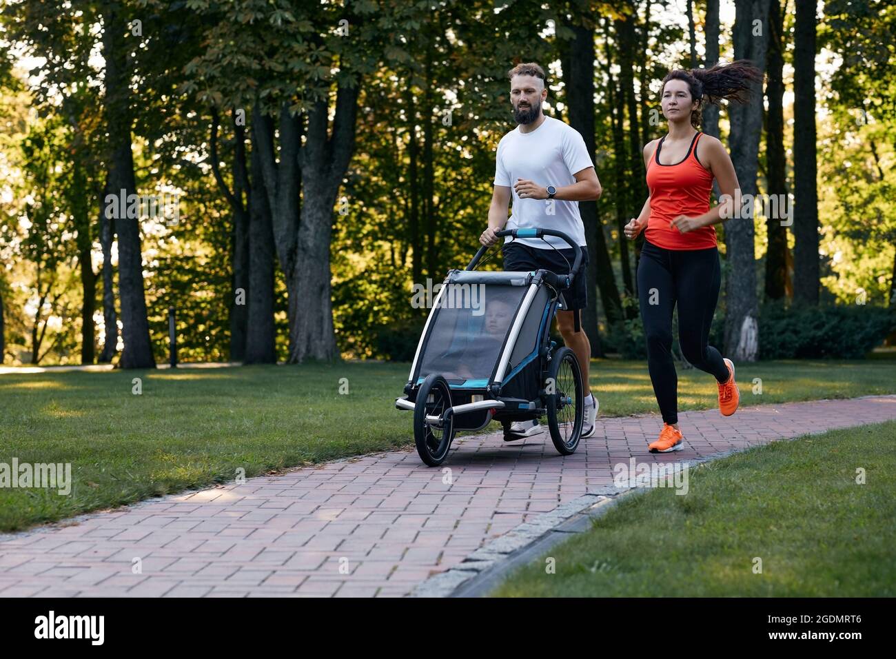 Une famille avec un enfant court avec une poussette à jogging dans un parc de la ville Banque D'Images