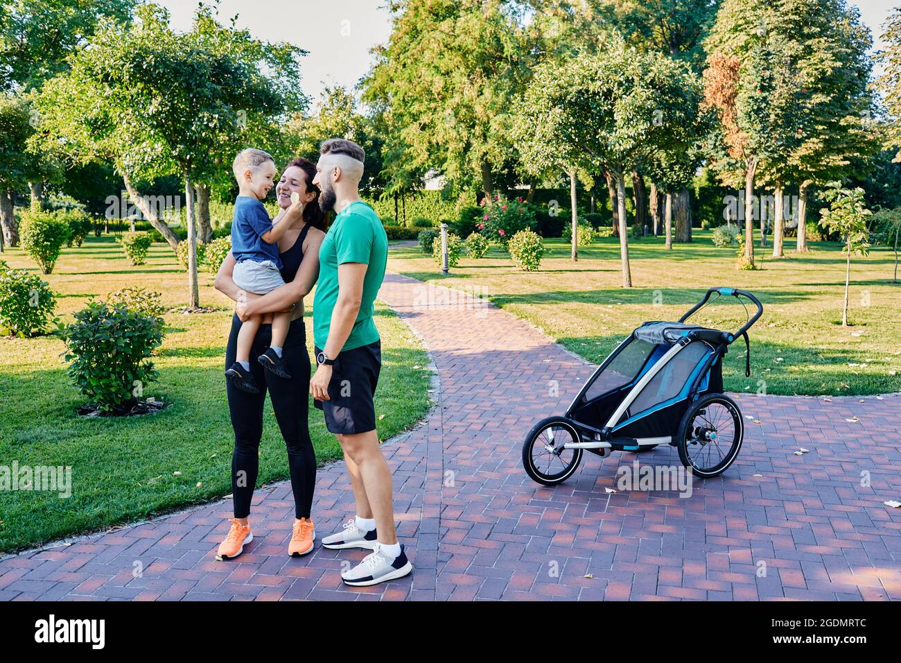 Famille active après avoir fait de l'exercice et de la course avec une poussette de jogging dans le parc de la ville. Couple heureux avec son pendant l'entraînement Banque D'Images