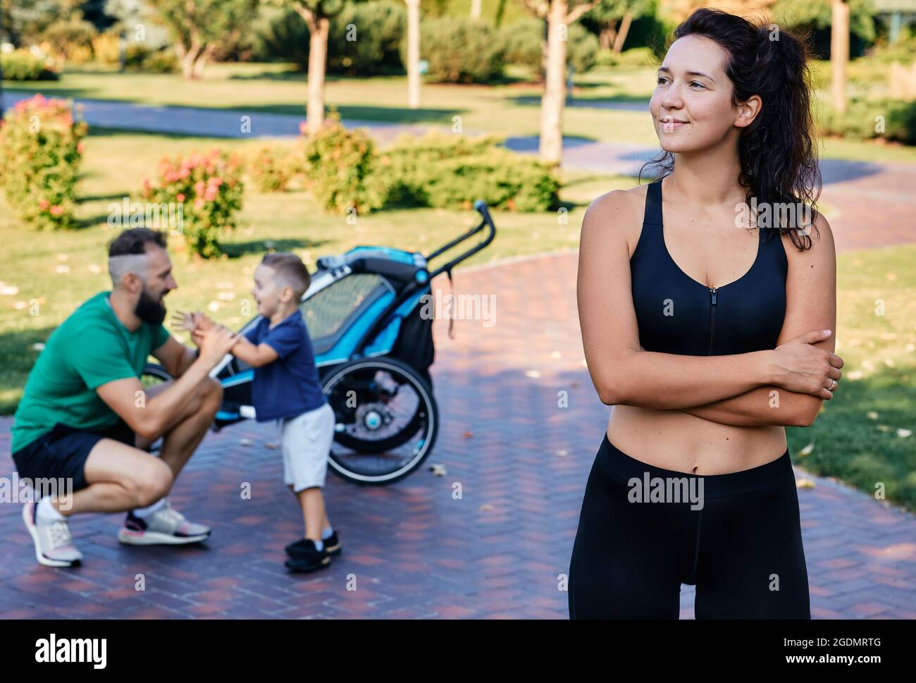 Portrait d'une maman sportive portant des vêtements de sport sur l'arrière-plan de son mari et de son fils après un entraînement et des exercices dans un parc de la ville. Bonne famille sportive Banque D'Images