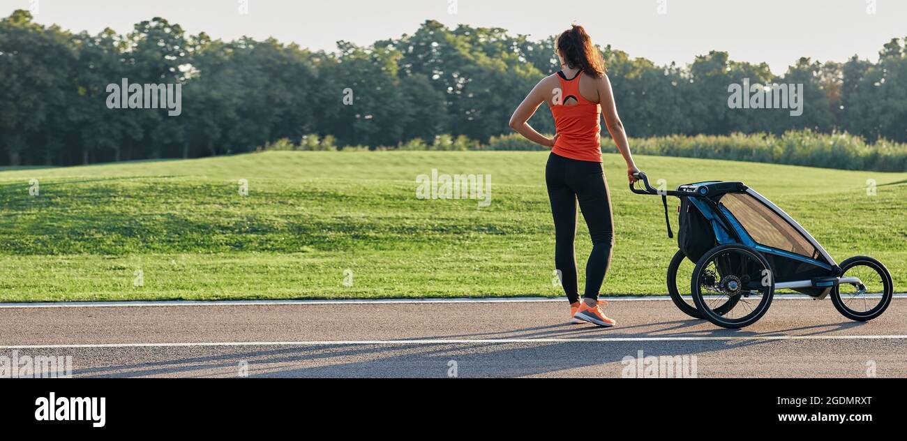 La mère active dans les vêtements de sport utilise une poussette de jogging pour courir au parc. Bonne femme s'amusant pendant l'entraînement en plein air. Publicité pour poussettes de jogging Banque D'Images