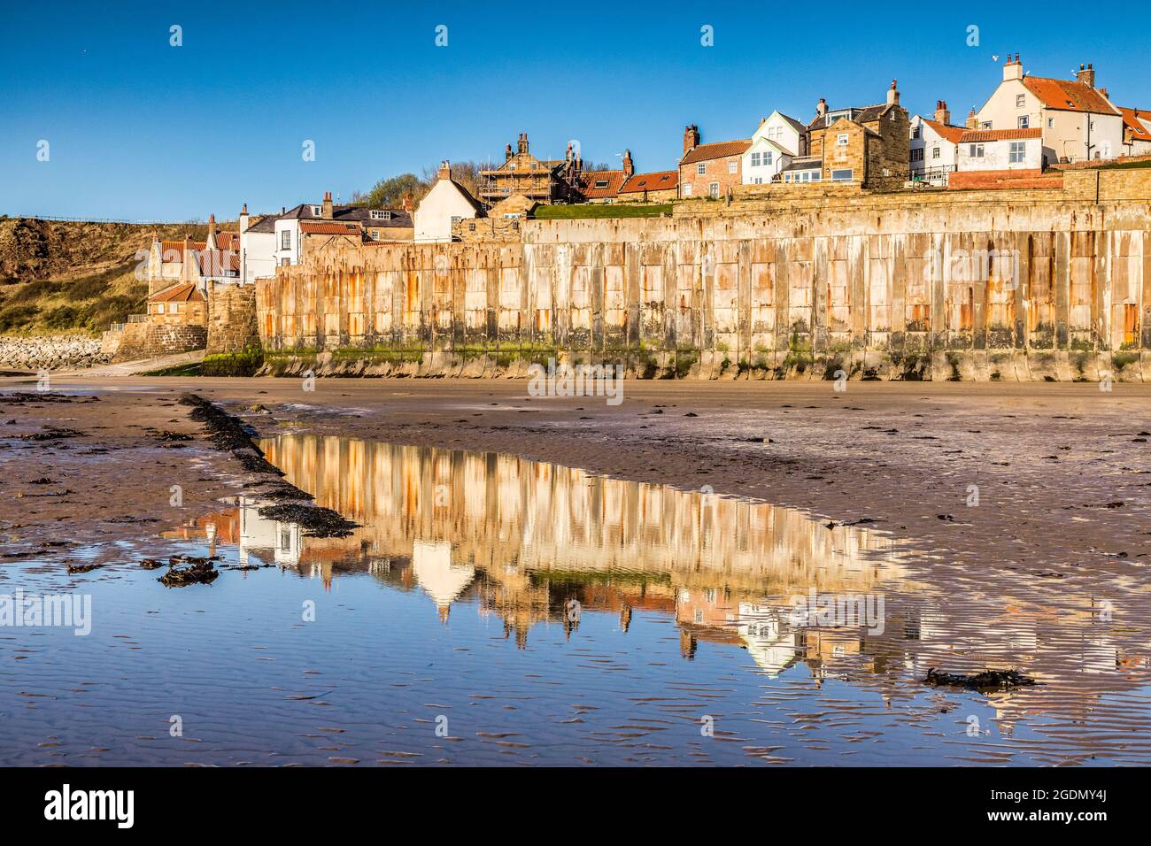 Le mur de mer et le village de Robin Hood Bay, dans le North Yorkshire, depuis l'estran le matin du printemps, avec des reflets dans une piscine. Banque D'Images