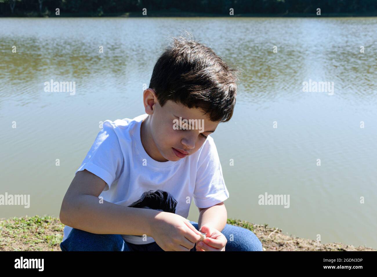 enfant de 8 ans mettant l'appât sur le crochet pour pêcher un matin ensoleillé. Banque D'Images