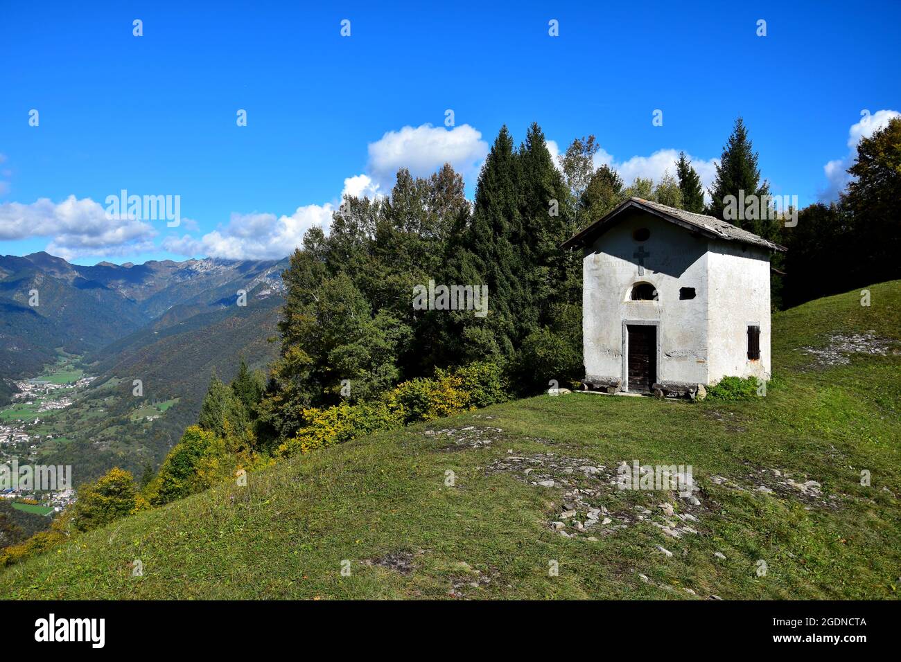 La petite chapelle de San Martino sur le mont Corno lors d'une belle journée d'automne claire. Sur la gauche quelques petites villes dans une vallée. Trentin, Italie. Banque D'Images