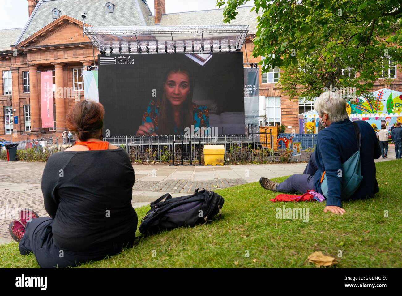 Édimbourg, Écosse, Royaume-Uni. 14 août 2021. Vues sur le jour d'ouverture du Festival International du livre d'Édimbourg à un nouveau lieu au Edinburgh College of Art. Ayant quitté son ancien site aux jardins de Charlotte Square, le Festival du livre s'est déplacé dans une cour au Edinburgh College of Art. Le nombre de visiteurs était probablement faible à l'heure du déjeuner en raison de de nombreux événements sont déplacés vers des diffusions en ligne. Photo : le grand écran de la cour montre des interviews en direct avec des auteurs. Iain Masterton/Alamy Live News. Banque D'Images