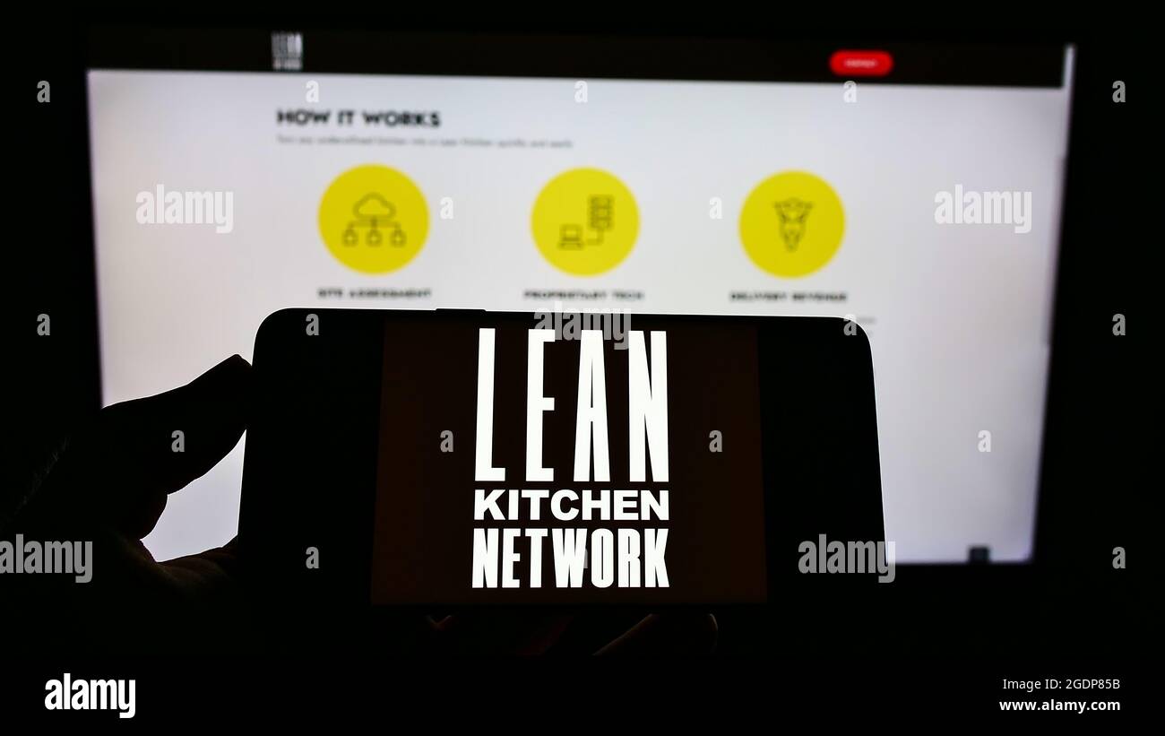 Personne tenant un téléphone portable avec le logo de la société britannique Lean Kitchen Network Limited (LKN) à l'écran en face de la page Web. Mise au point sur l'affichage du téléphone. Banque D'Images