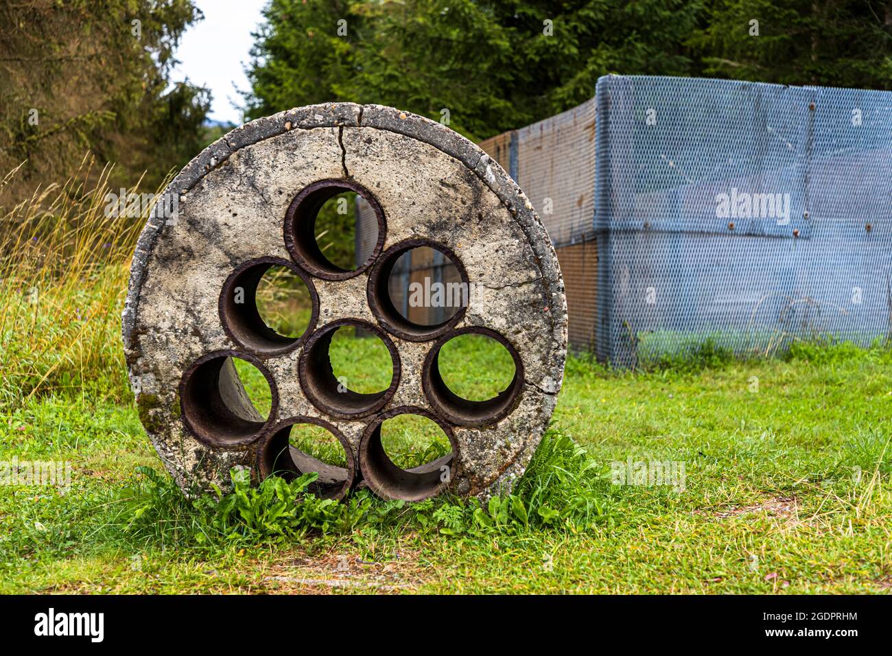 Un disque circulaire en béton muni de sept tuyaux – une barrière de tuyaux, appelée ainsi – gît dans l’herbe du Grenzmuseum Sorge (musée frontalier), Saxe-Anhalt, Allemagne. De telles barrières bloquaient les ruisseaux coulant sous la clôture frontalière contre toute personne plongeant pour s’échapper, tout en laissant l’eau s’écouler. Banque D'Images