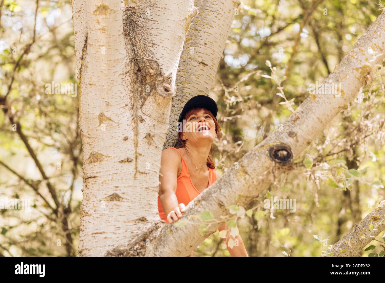 Femme assise dans un arbre en riant avec une expression heureuse Banque D'Images