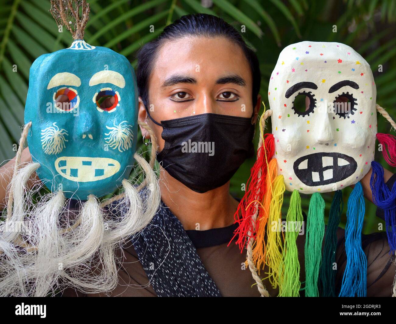 Un jeune homme artiste mexicain montre deux de ses masques de cérémonie et porte un masque chirurgical noir pendant la pandémie du coronavirus. Banque D'Images