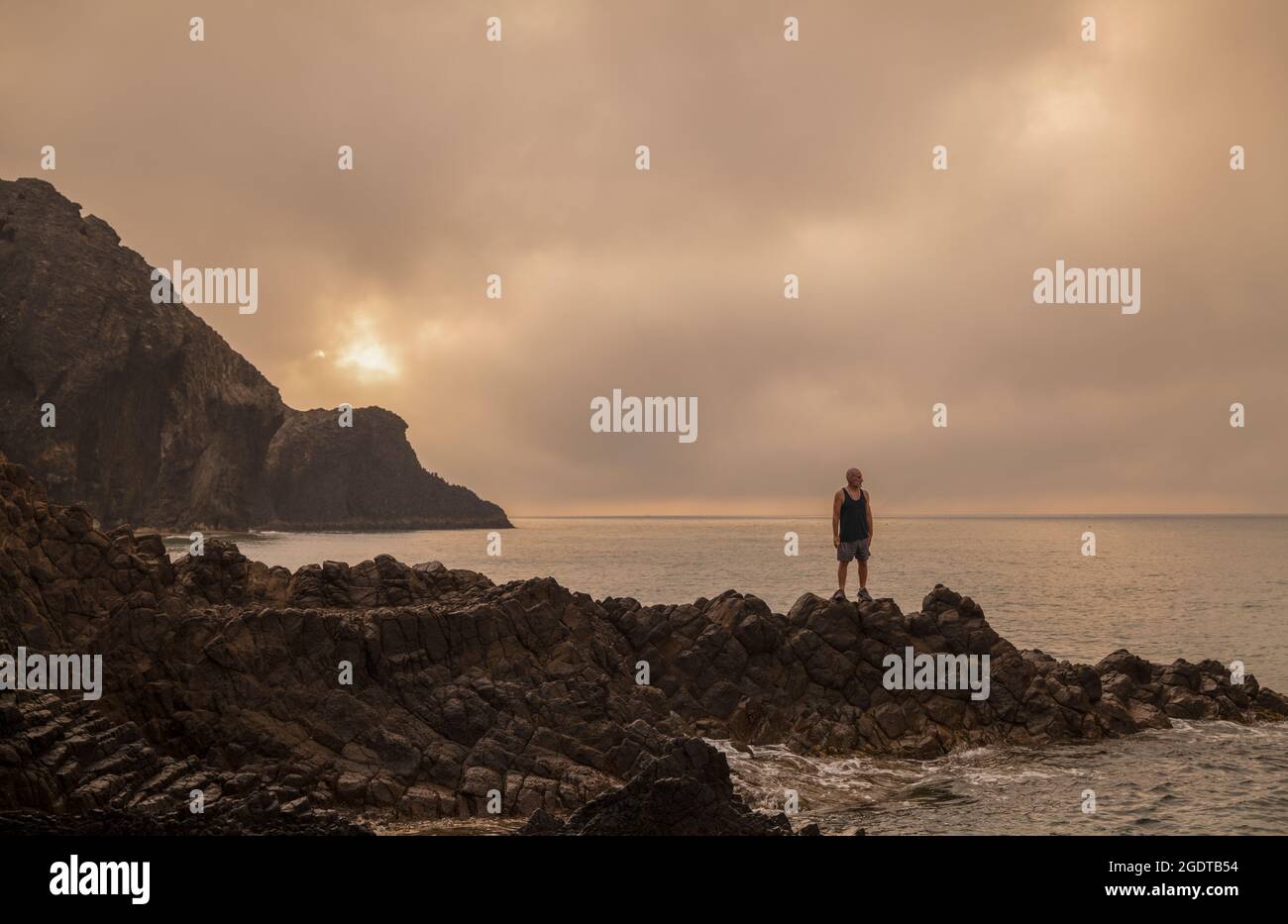 Homme debout sur le rocher et regardant la vue sur la plage pittoresque au lever du soleil Banque D'Images