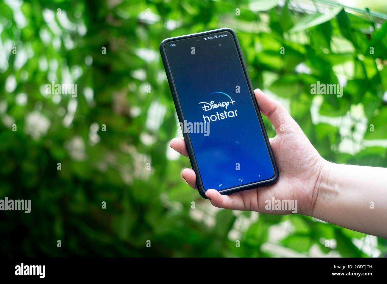 Téléphone mobile smartphone avec la populaire application de streaming OTT hotstar Disney plus en Inde. Tenue par une jeune femme à l'extérieur avec des plantes de fond Banque D'Images