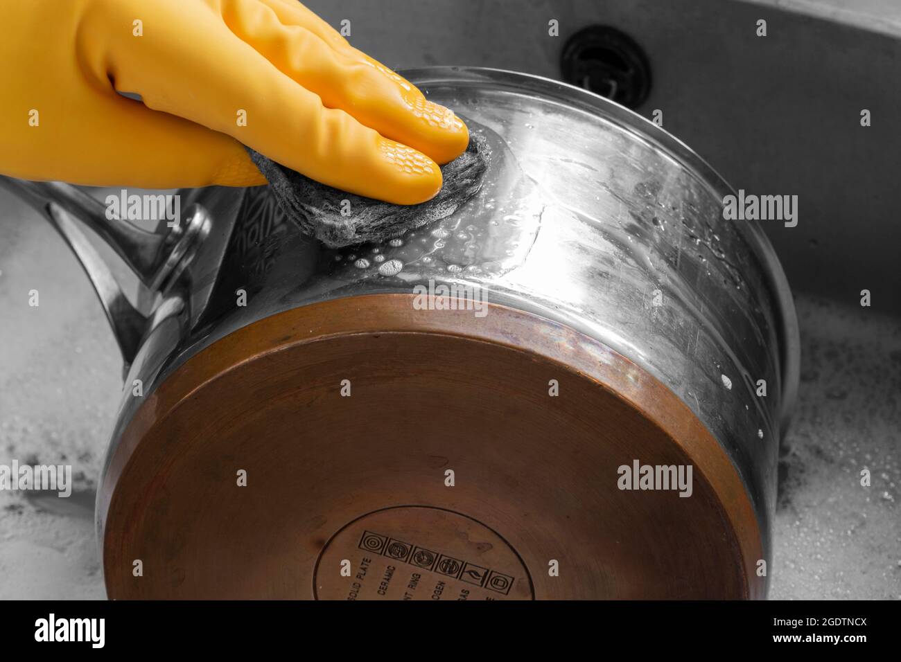 Personne, portant des gants en caoutchouc, nettoyant une casserole en acier inoxydable et en cuivre avec un tampon métallique. Banque D'Images