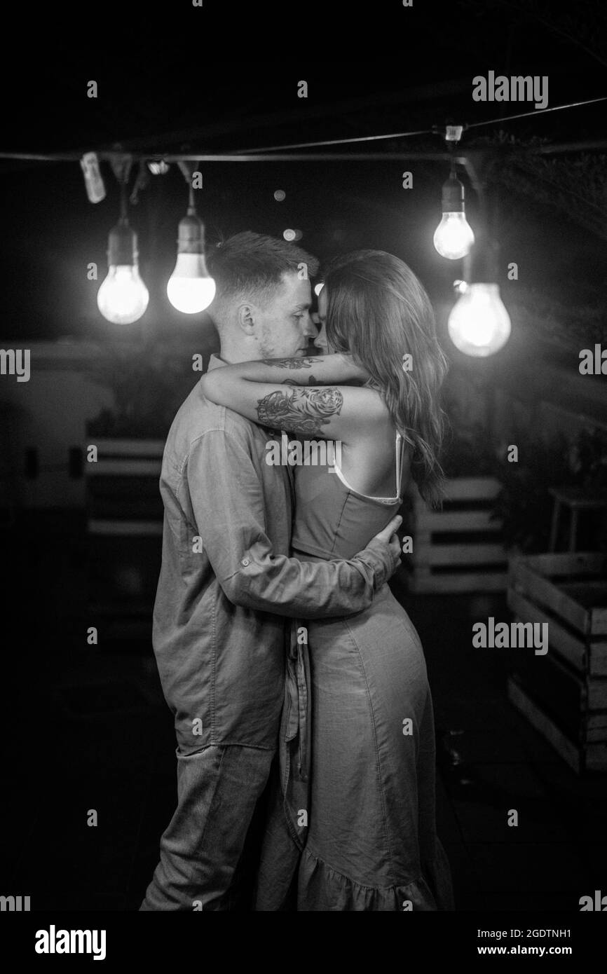 Portrait d'un couple aimant debout dans la barre sombre avec des lanternes, câliner et regarder dans les yeux. Image en noir et blanc. Photo de haute qualité Banque D'Images