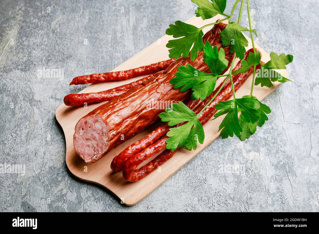 Saucisse fumée décorée de feuilles de persil sur fond gris en pierre. Banque D'Images