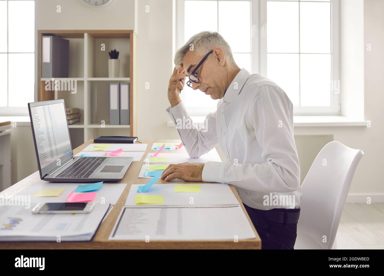 Homme d'affaires senior occupé et concentré regardant des notes sur des autocollants colorés couchés sur la table. Banque D'Images