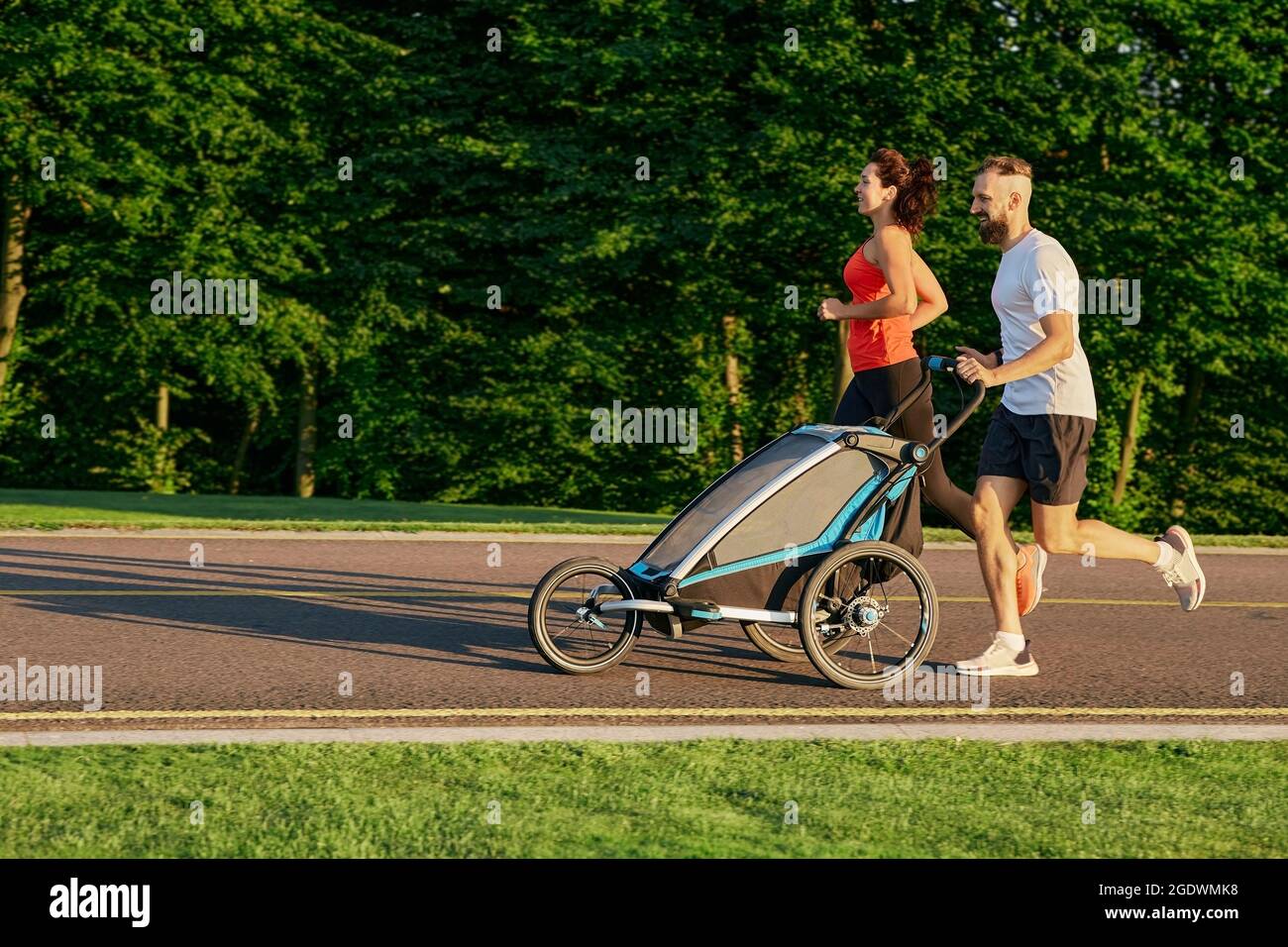 couple de course avec enfant dans la poussette de jogging dans le parc public au lever du soleil. Course matinale pour toute une famille Banque D'Images