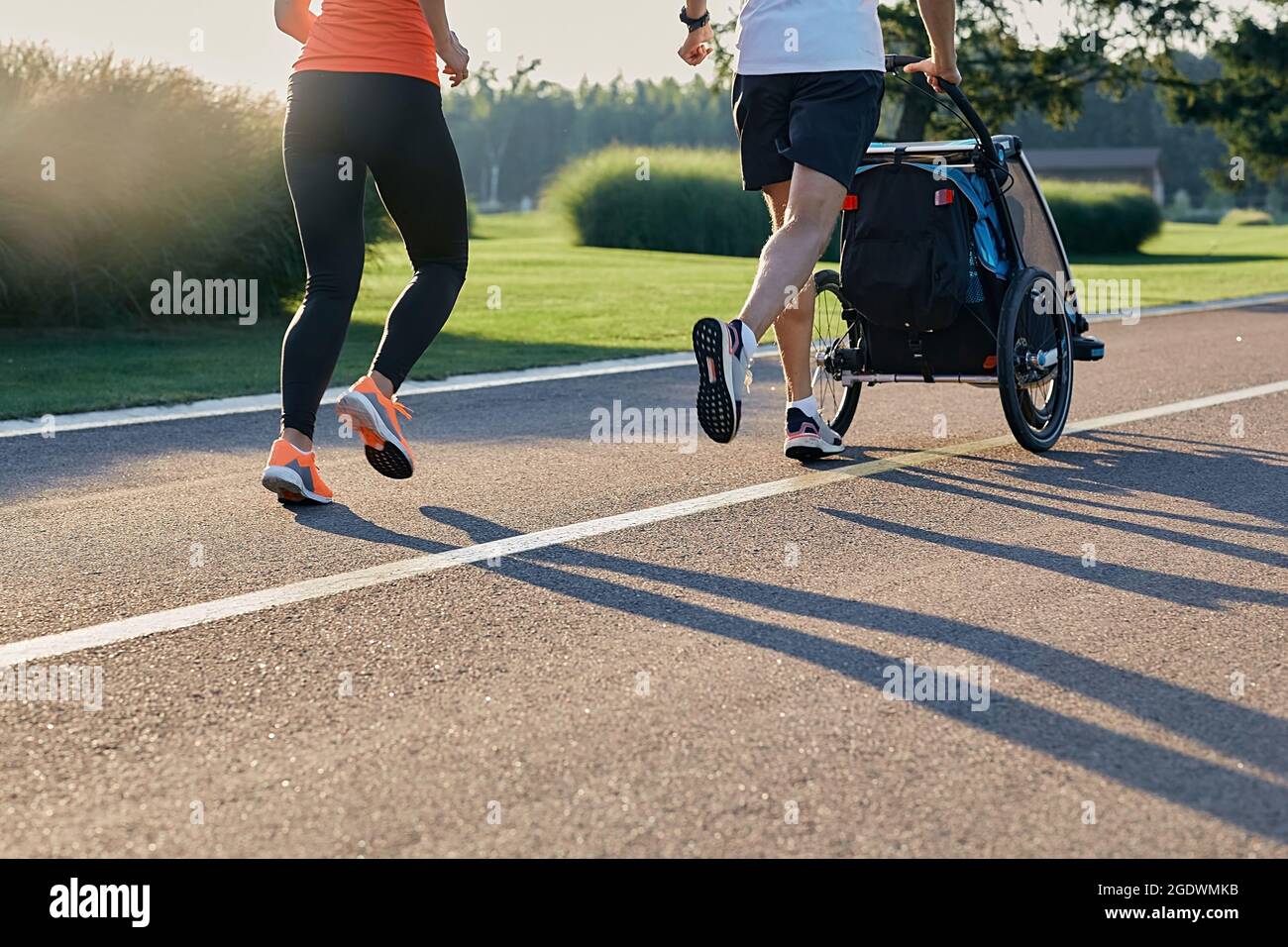courir jeune famille avec poussette de jogging bébé en mouvement profiter de l'entraînement et la journée d'été dans le parc de la ville. Vue arrière Banque D'Images