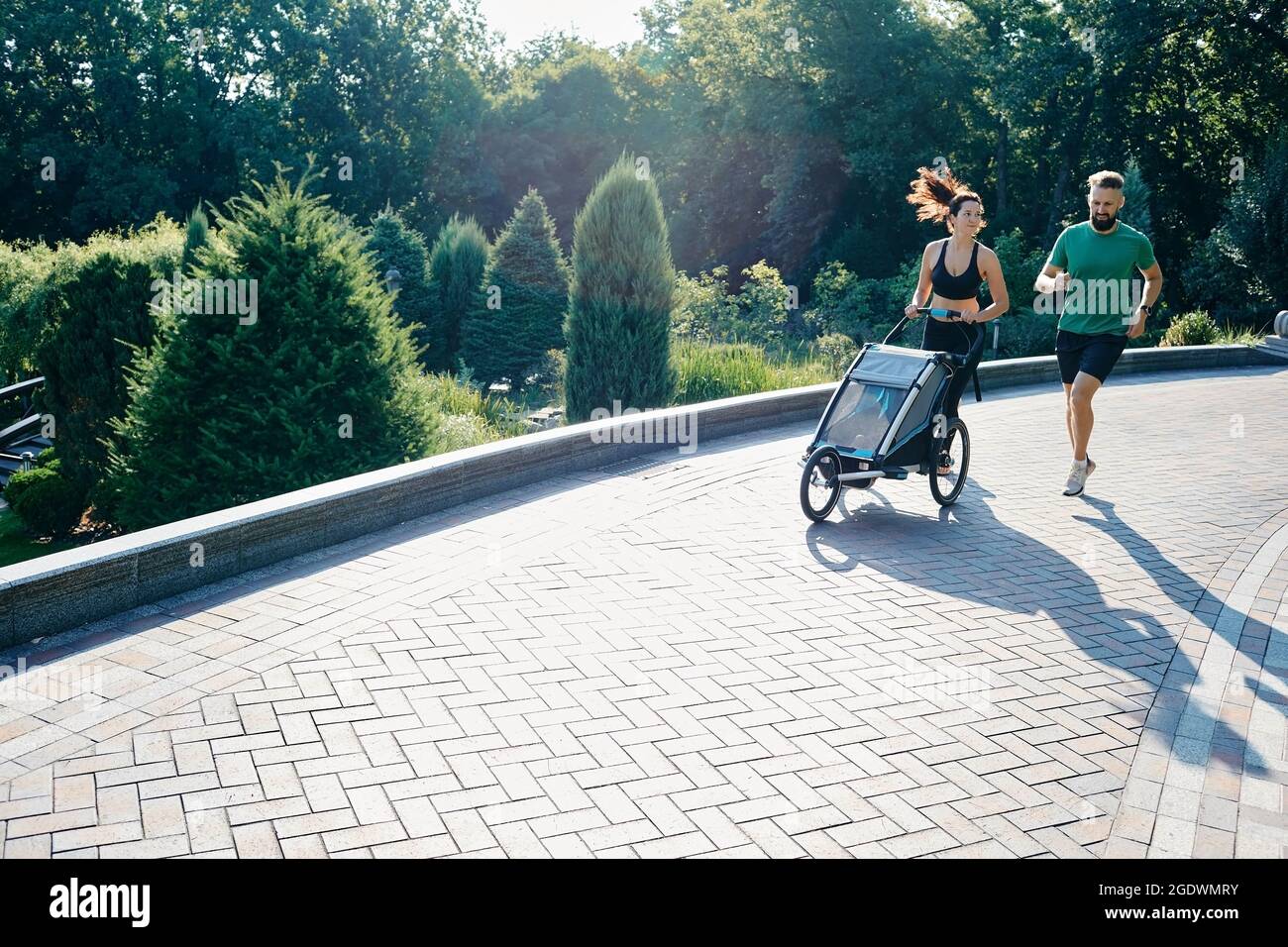 Une famille avec un enfant court avec une poussette à jogging dans un parc de la ville Banque D'Images