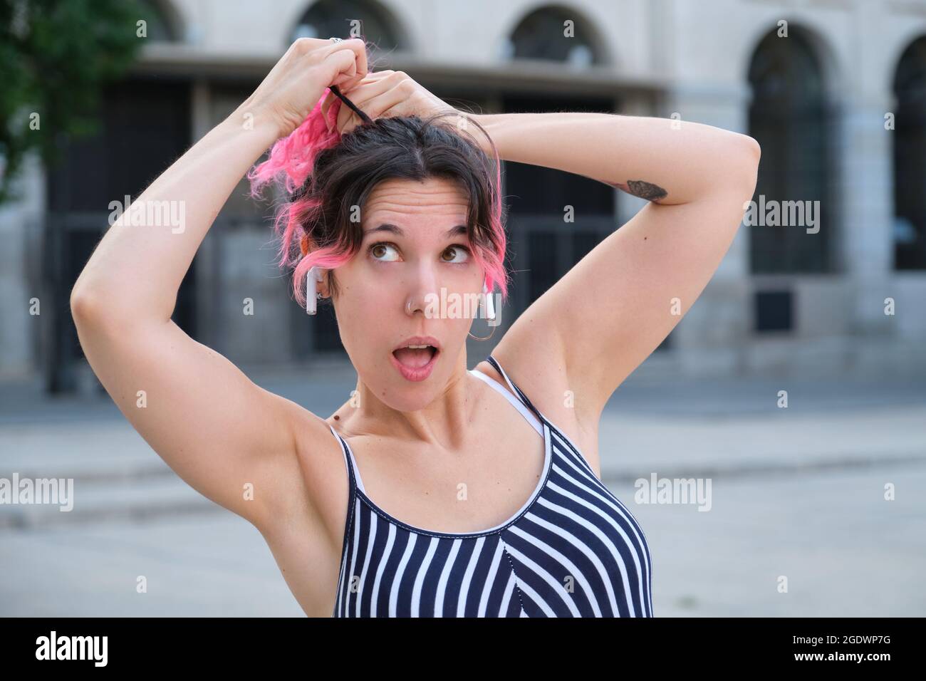 Jeune femme caucasienne avec cheveux roses et oreillettes sans fil faisant une queue de cheval. Banque D'Images