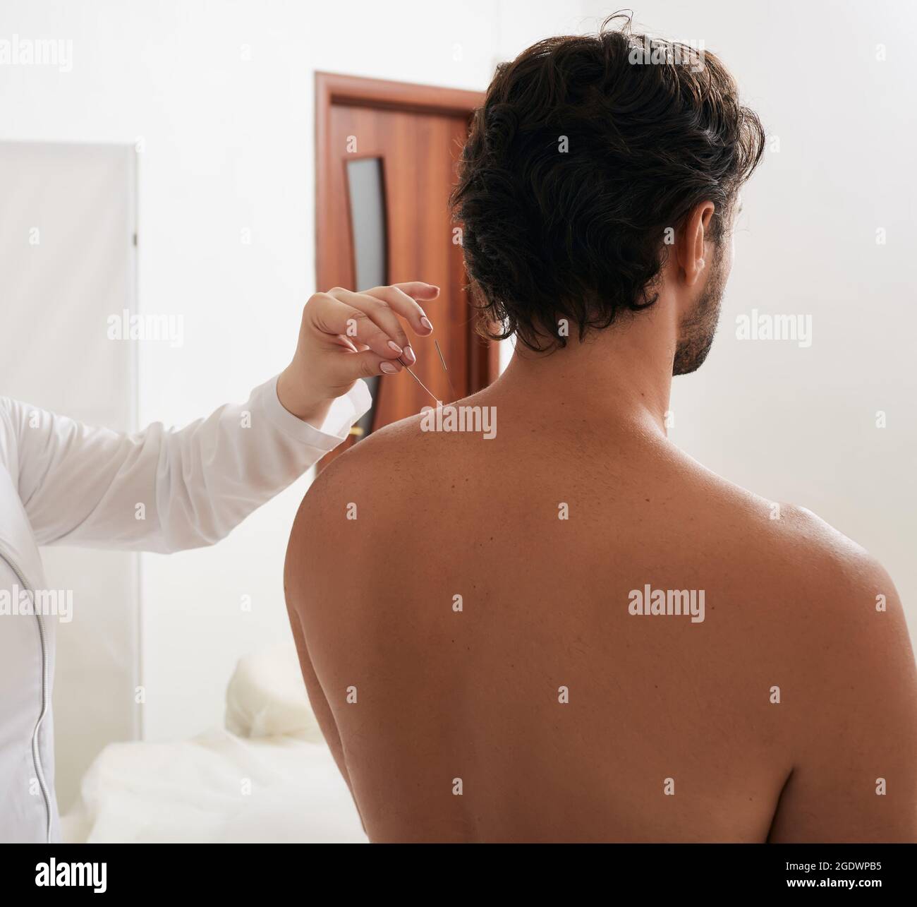 La main du réflexologiste avec l'aiguille d'acupuncture tout en insérant l'aiguille dans le point spécial sur le corps de l'homme méridiens pour le traitement. Vue arrière Banque D'Images