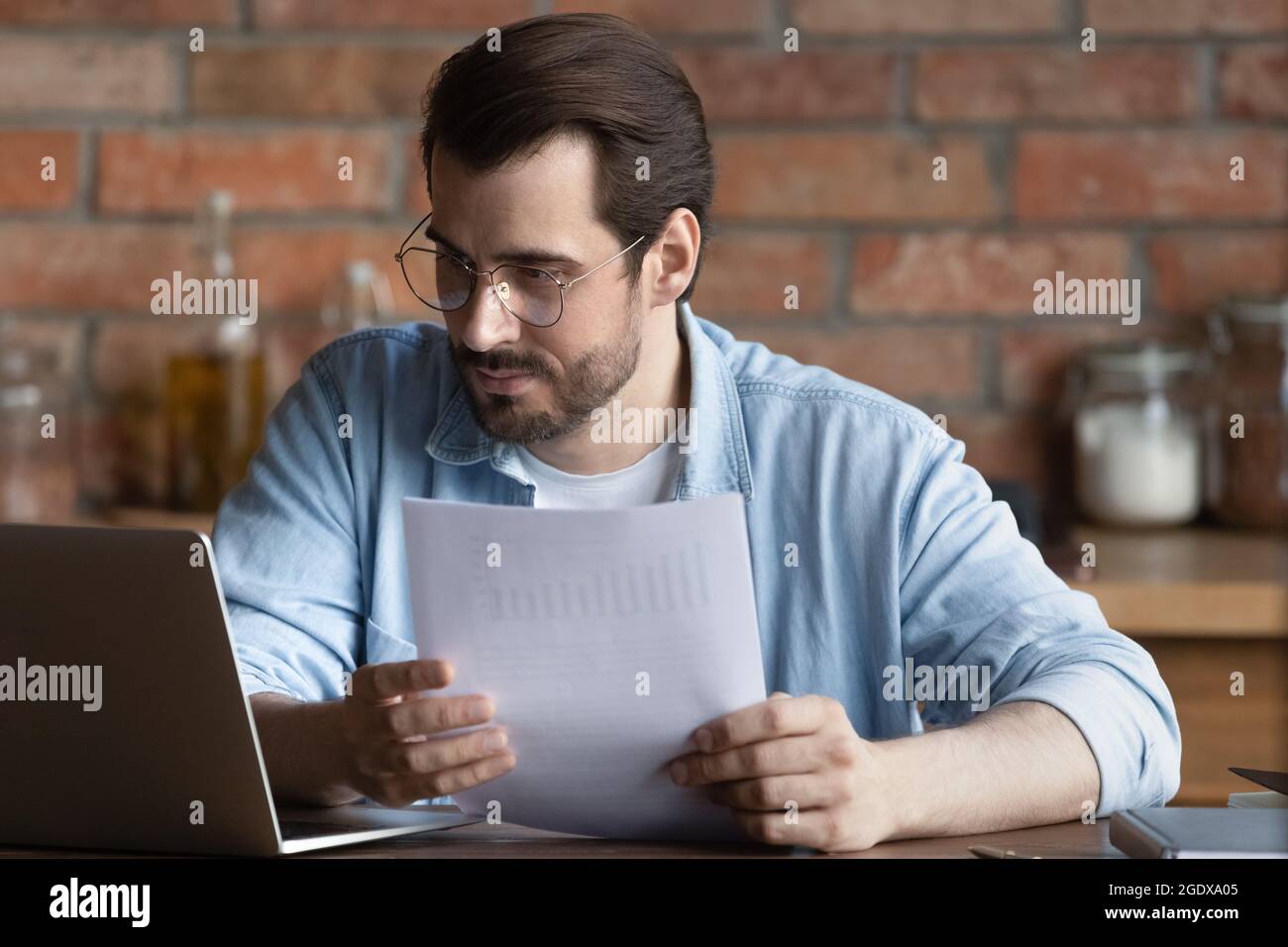 Un homme millénaire sérieux travaille sur un ordinateur portable avec des documents administratifs Banque D'Images