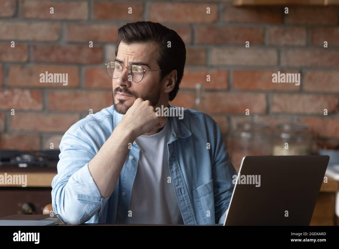 Un jeune homme pensif travaille sur la pensée d'un ordinateur portable Banque D'Images
