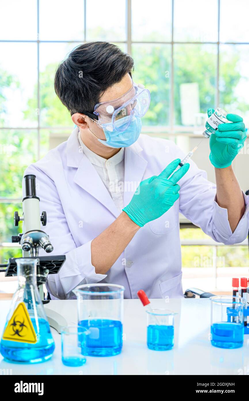 Un scientifique mâle portant une combinaison de protection contenant un vaccin contre le coronavirus et travaillant avec de nombreux équipements de laboratoire pour la recherche d'un vaccin en laboratoire. Rés. Médicale Banque D'Images