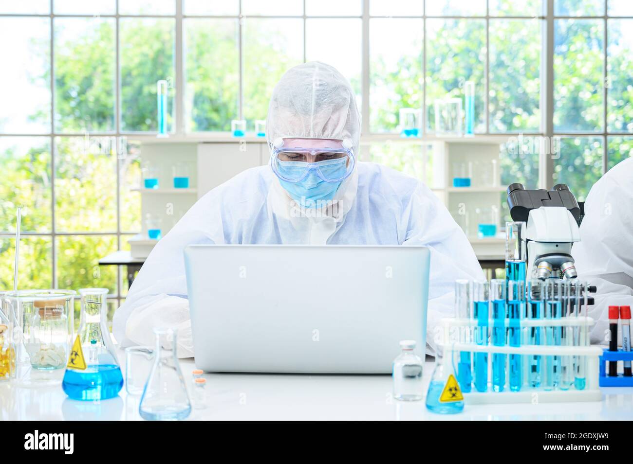 Homme scientifique portant une combinaison de protection travaillant avec un ordinateur portable et de nombreux équipements de laboratoire pour la recherche en laboratoire. Chercheur spécialisé en médecine. Banque D'Images