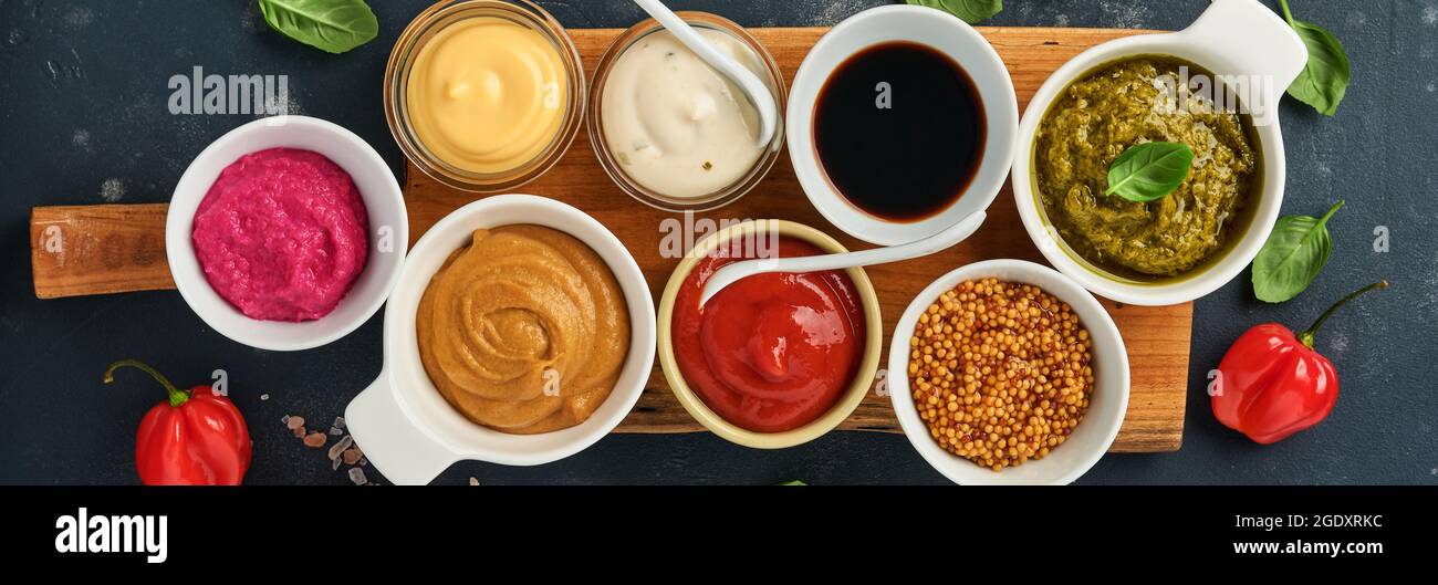 Ensemble de sauces dans des bols - ketchup, mayonnaise, moutarde, sauce soja, sauce barbecue, pesto, chimichurri, grains de moutarde sur fond de pierre sombre. Vue de dessus cop Banque D'Images