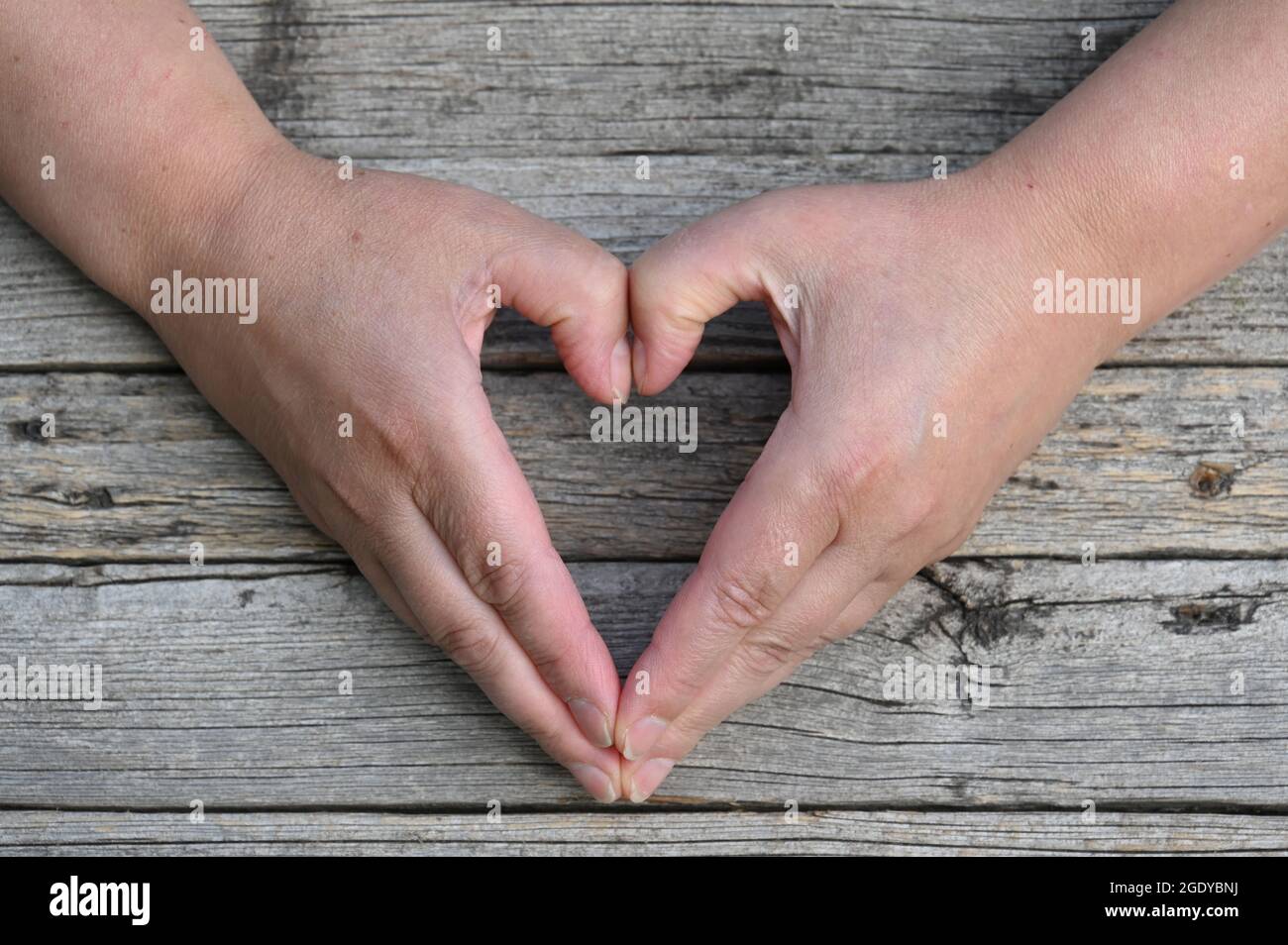 Deux mains sur un fond rustique en bois forment un coeur Banque D'Images