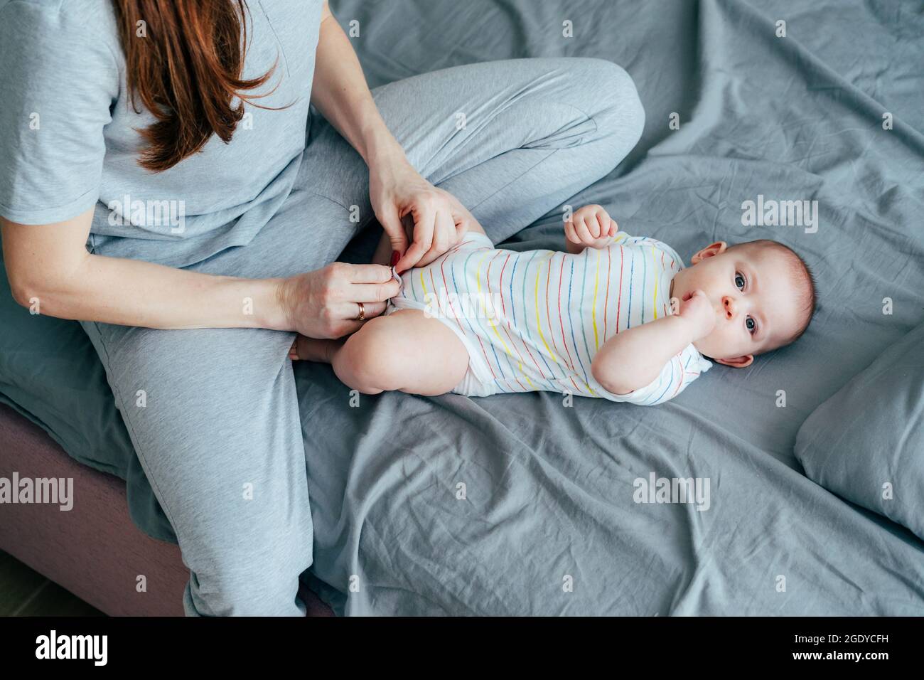 Maman habille le bébé allongé sur la literie dans un body d'été Banque D'Images