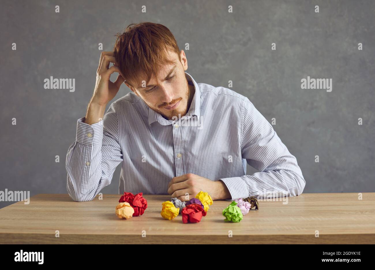 Homme assis à un bureau avec des boules de papier froissés et pensant dur essayer de trouver une idée Banque D'Images