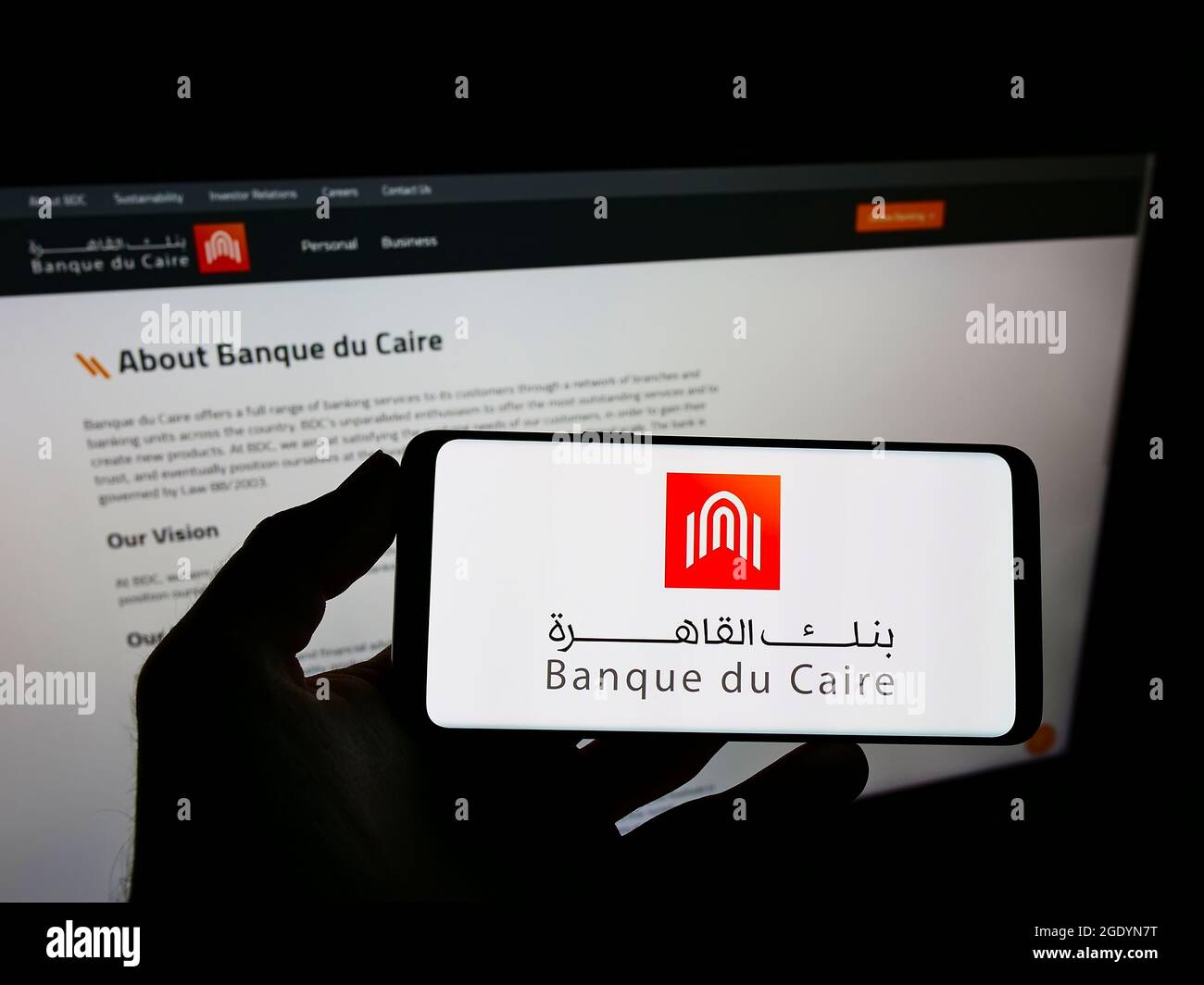 Personne tenant un téléphone portable avec le logo de la banque égyptienne Banque du Caire à l'écran en face de la page Web d'affaires. Mise au point sur l'affichage du téléphone. Banque D'Images