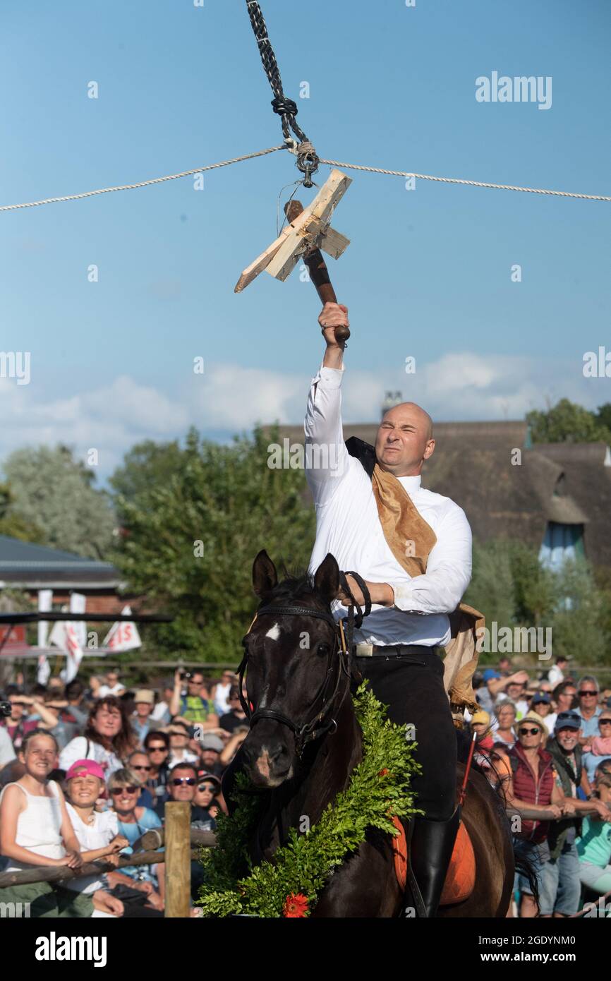 Ahrenshoop, Allemagne. 15 août 2021. Le « roi du canon » 2021, Alexander Kluge de Wustrow, passe sous le canon en bois et frappe un morceau de bois pendant la coupe traditionnelle du canon. La fête du tonneau est une ancienne coutume dans laquelle les cavaliers concourent à un galop et avec un club dans leurs mains. Credit: Stefan Sauer/dpa/ZB/dpa/Alay Live News Banque D'Images