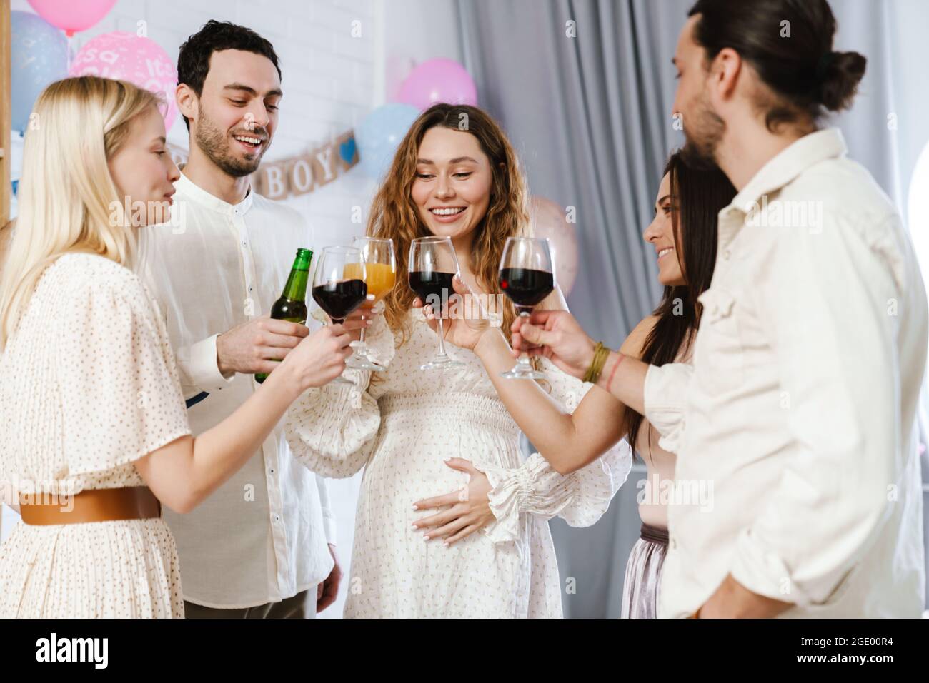Jeune femme enceinte heureuse buvant avec ses amis pendant la fête de révélation de sexe à l'intérieur Banque D'Images
