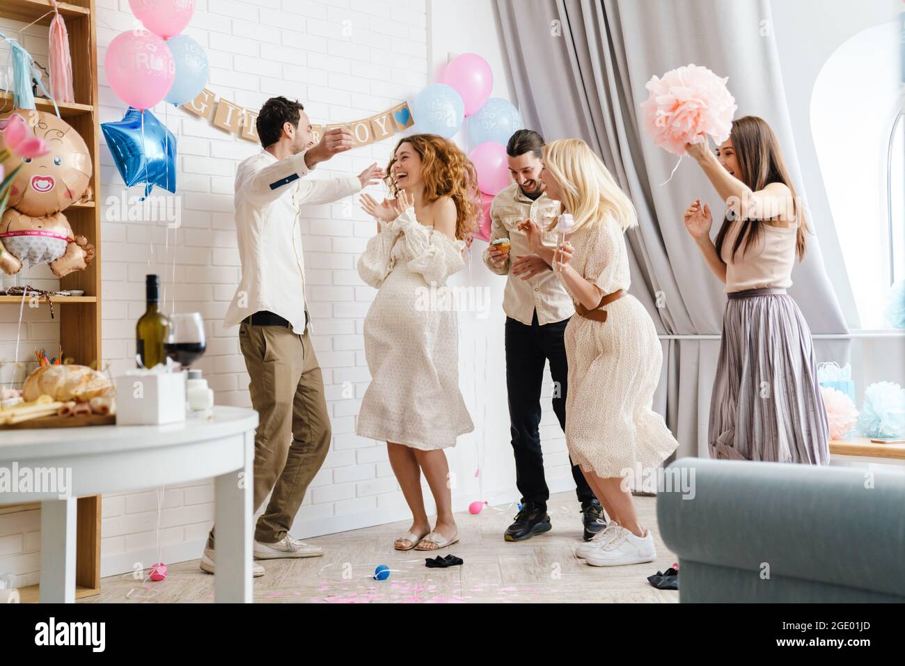 Jeune couple excité avec leurs amis riant et dansant pendant la fête de révélation de genre à l'intérieur Banque D'Images