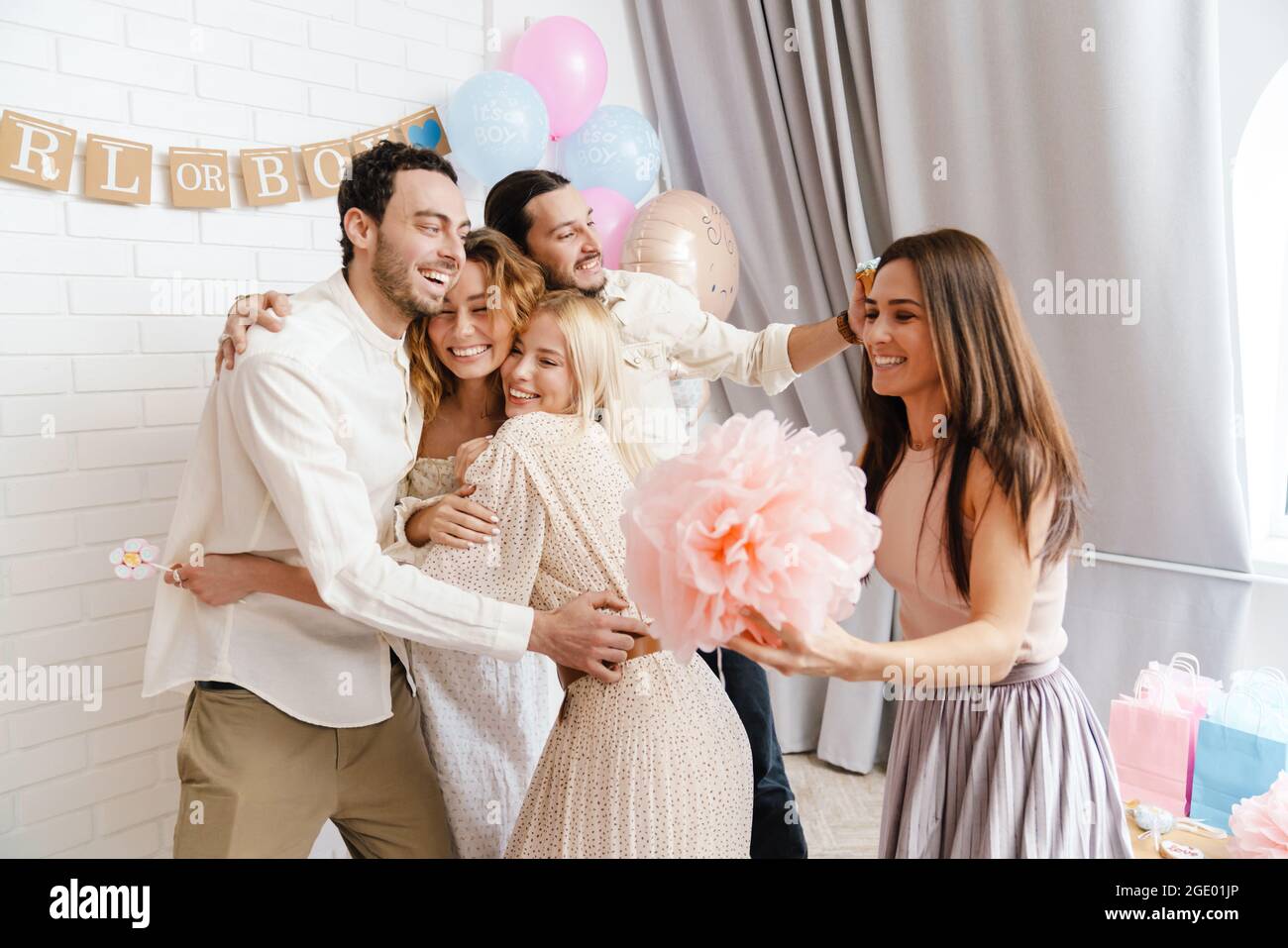 Un jeune couple enthousiaste qui s'embrasse avec ses amis pendant la fête de révélation de genre à l'intérieur Banque D'Images
