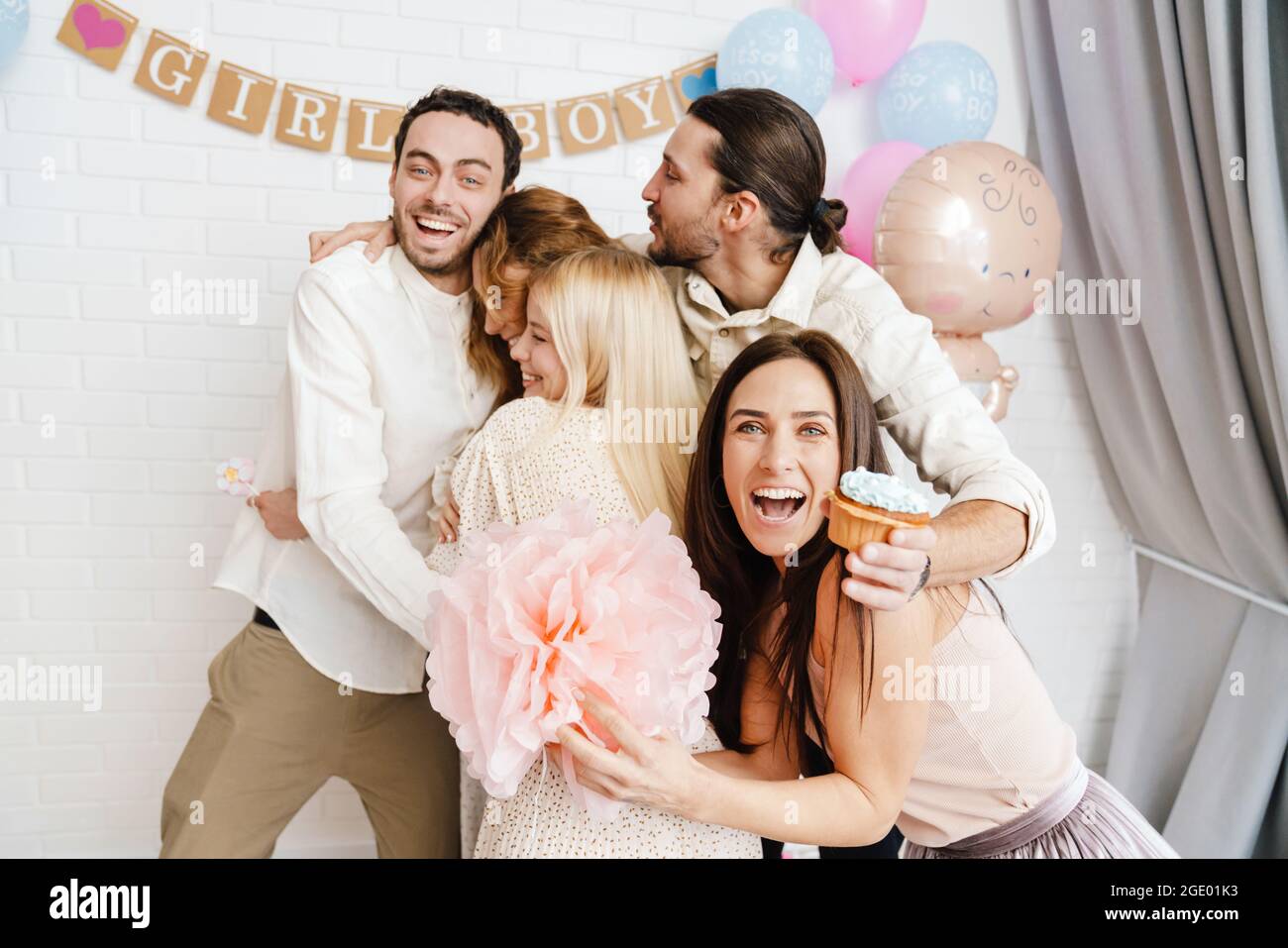 Un jeune couple enthousiaste qui s'embrasse avec ses amis pendant la fête de révélation de genre à l'intérieur Banque D'Images