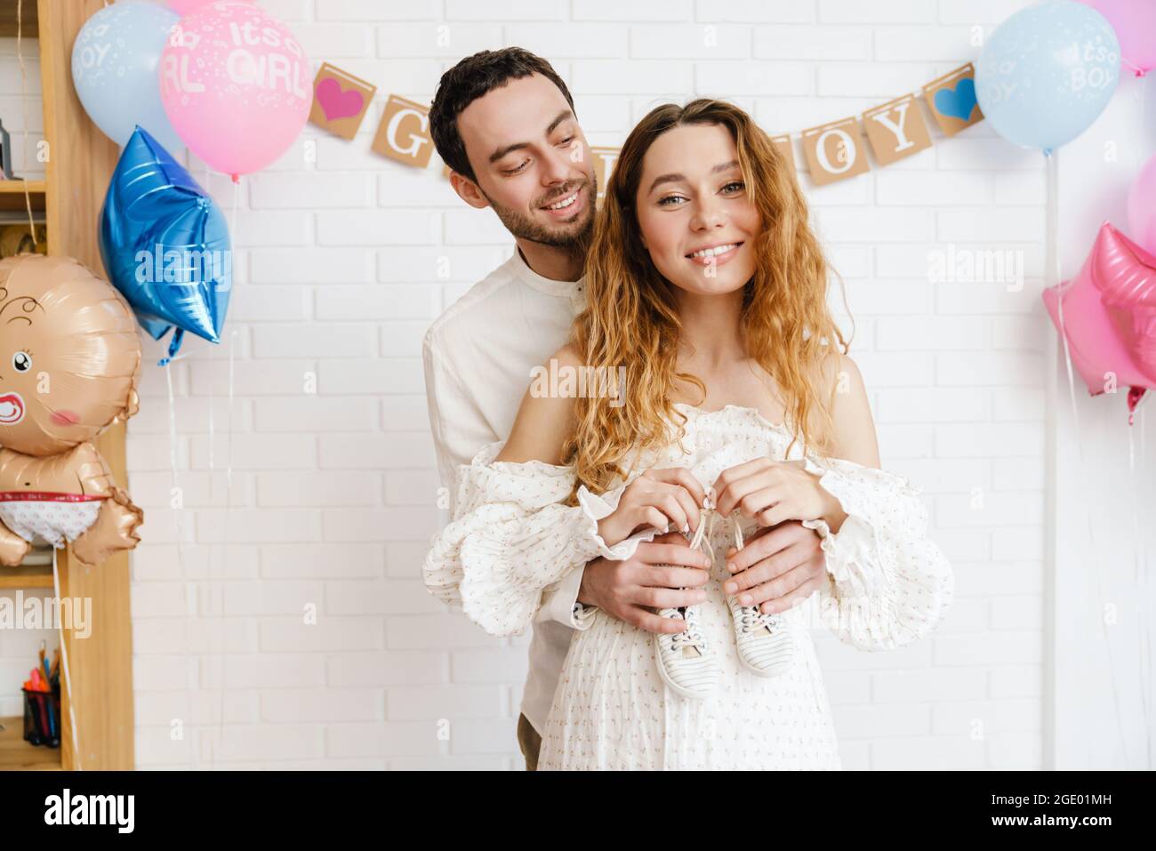 Jeune couple heureux posant avec des chaussures de bébé pendant la fête de révélation de sexe à l'intérieur Banque D'Images