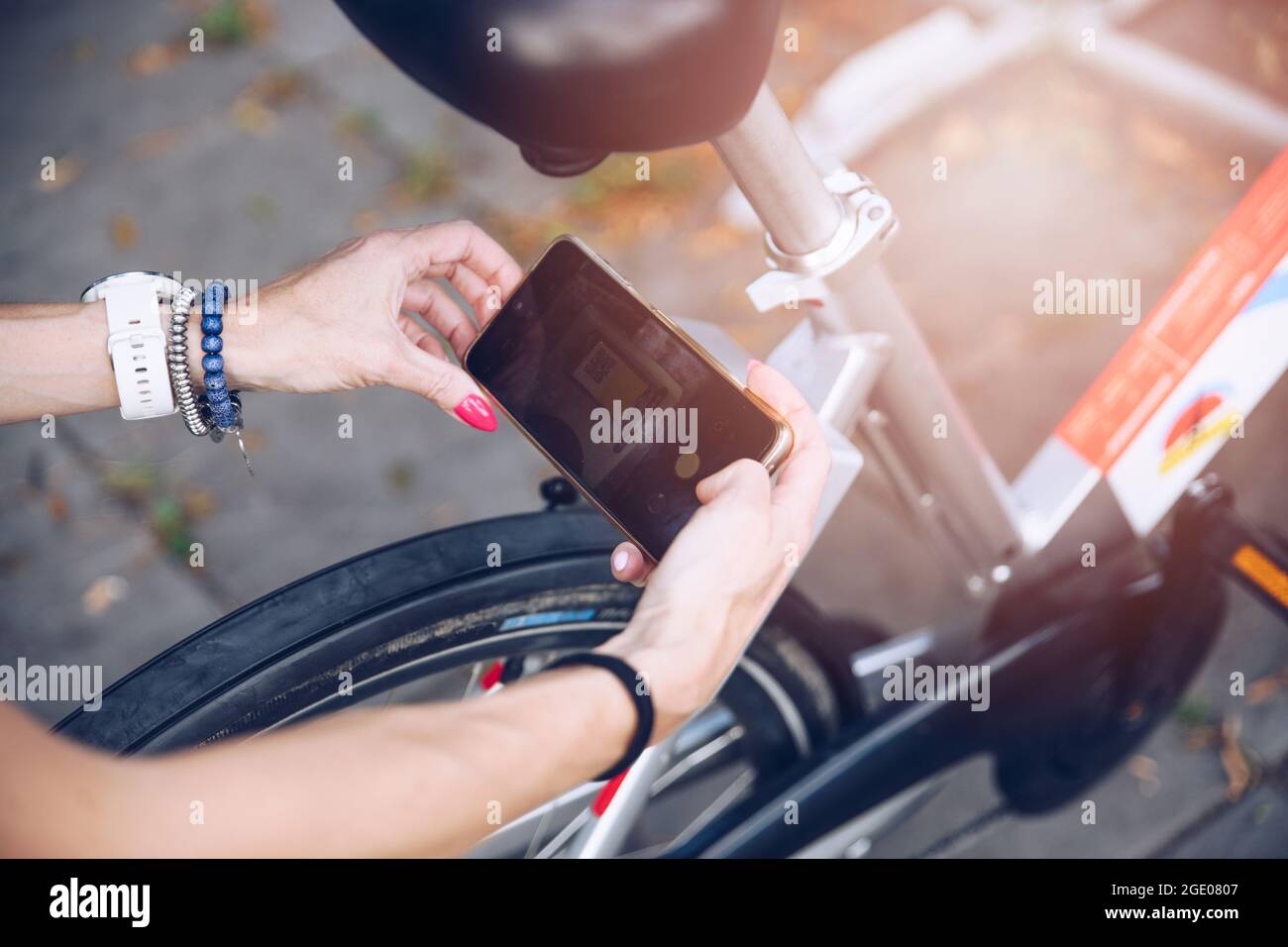 Fille dans la ville d'été utilisant le téléphone pour déverrouiller une ville de vélo dans la ville. Banque D'Images