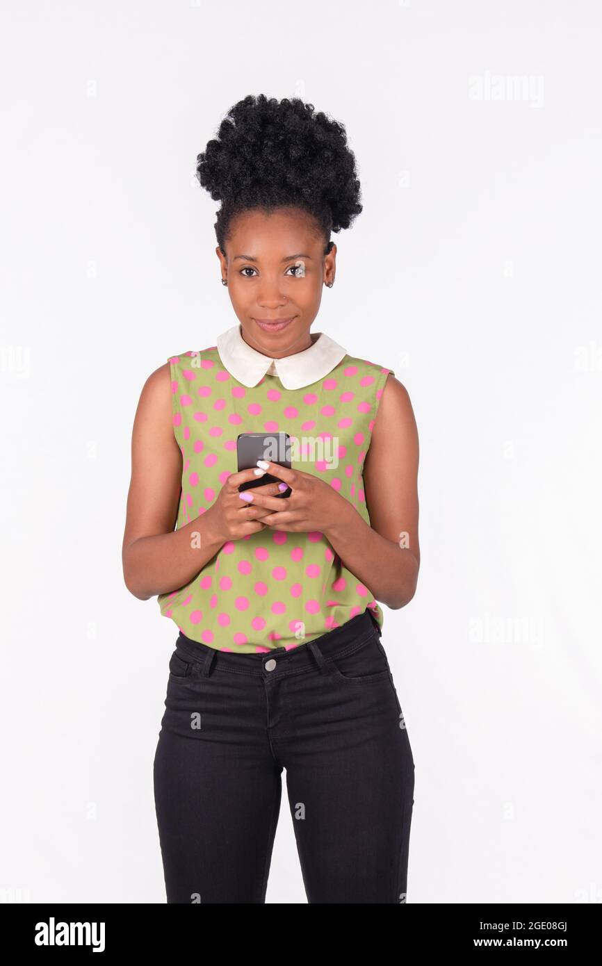 Une femme souriante de Latina tenant son téléphone près de sa poitrine tout en regardant la caméra, debout sur un arrière-plan clair Banque D'Images